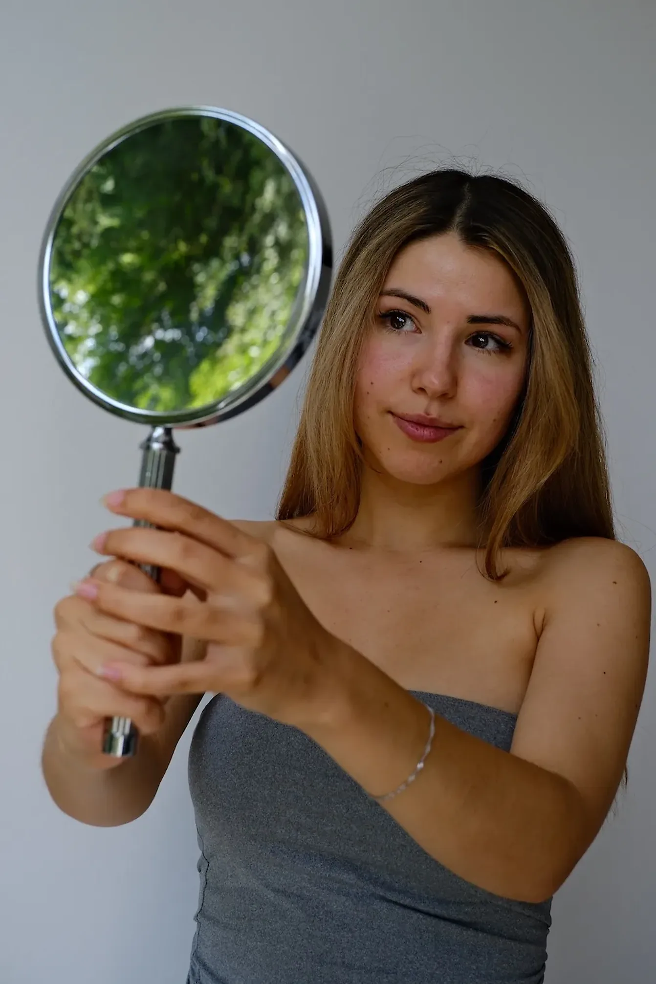 Frau mit langem Haar hält einen runden Handspiegel und betrachtet das Behandlungsergebniss ihrer Behandlung bei Skinthetics