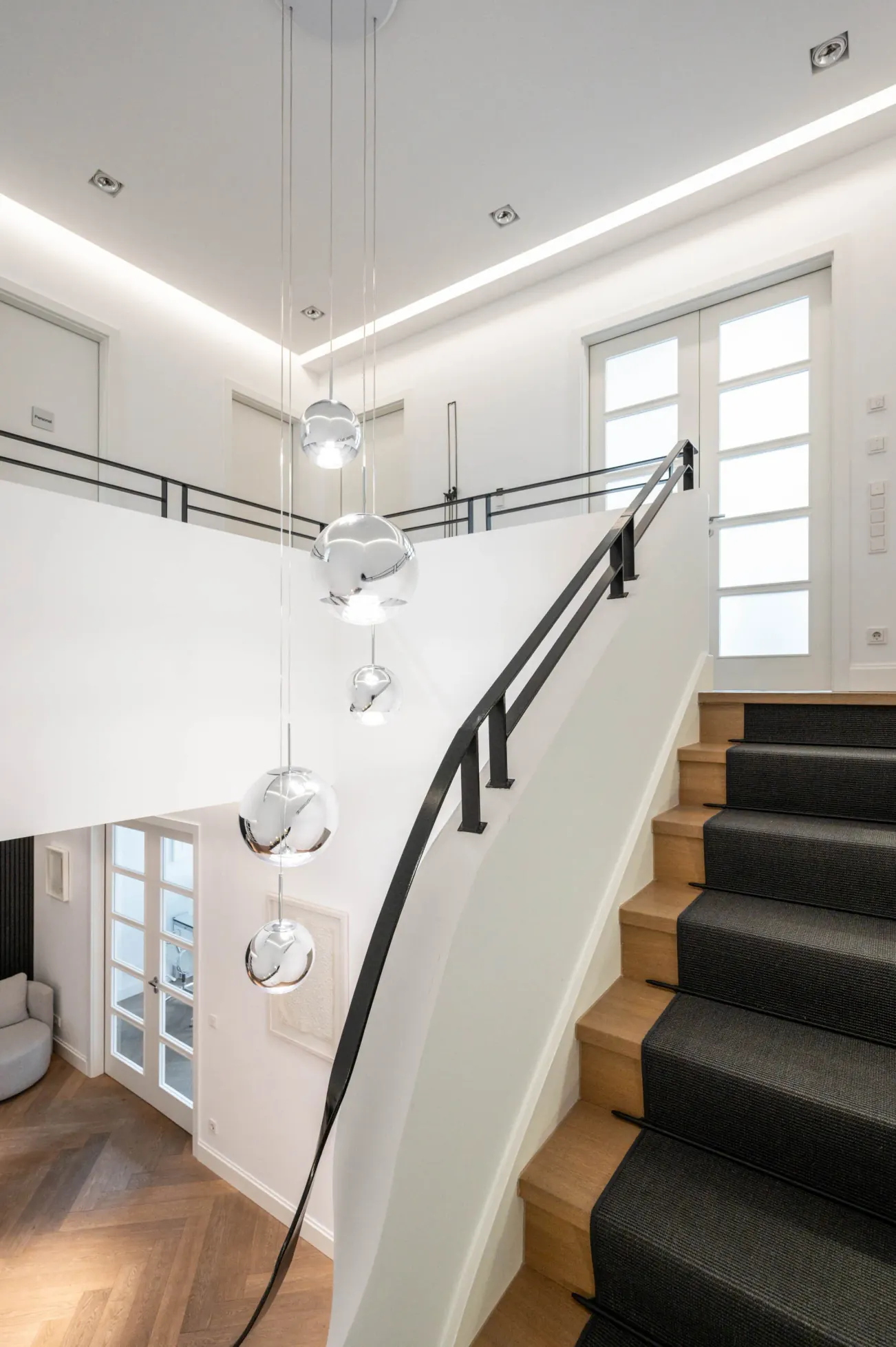 Practice interior: modern staircase with wooden steps and a black carpet runner, white walls and silver globe pendant lights.